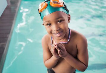 Ein Junge steht im SChwimmbad am Beckenrand uns trägt stotz eine Medaille