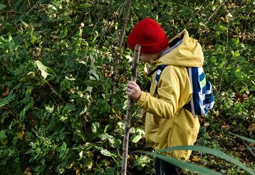 Junge läuft mit einem Stock in der Hand durchs Unterholz im Wald