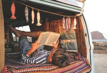Junge liest in einem Bully ein Buch, das Auto steht am Strand