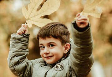 Junge im Wald mit Herbstlaub, hält zwei Blätter hoch