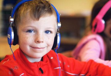 Junge mit rotem Pullover und blauem Kopfhörer lächelt in die Kamera
