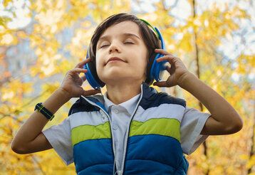 Junge mit Kopfhörern hört Musik, im Hintergrund Herbstlaub