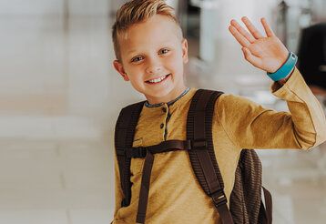 Junge mit Rucksack winkt zum Abschied