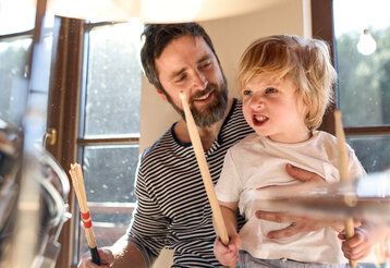 Kleiner Junge sitzt mit Vater am Schlagzeug
