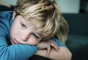 ein Junge guckt traurig in die Ferne, sein Kopf liegt auf seinen verschränkten Armen