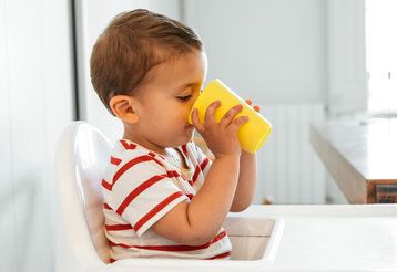 Junge sitzt in einem Hochstuhl und trinkt aus gelbem Becher