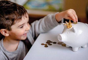 ein kleiner Junge wirft eine Münze ins Sparschwein