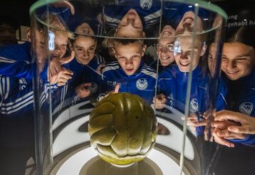 Jungs im Fußballdress betrachten Endspielball von 1954 im Fußballmuseum in Dortmund