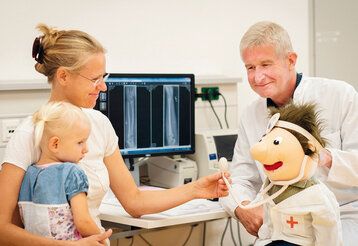 Mutter mit Kind im Arztgespräch, eine Arztpuppe ist auch dabei