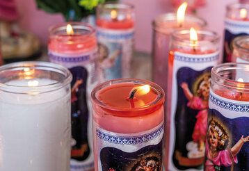 Kerzen in Glasbehältern mit Heiligenmotiven stehen nebeneinander