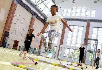 Mädchen springen in einer Turnhalle über kleine Hürden