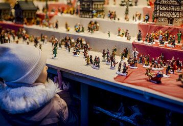 ein Kind steht an einem Weihnachtsmarktstand und guckt sich kleine Zinnfiguren an