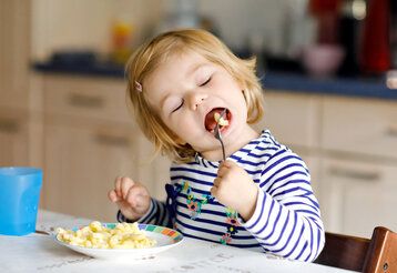 Kleinkind sitzt am Tisch isst Nudeln ohne Soße