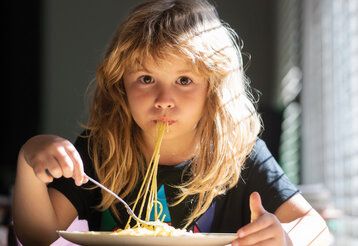 ein Kind isst Spaghetti und guckt in die Kamera