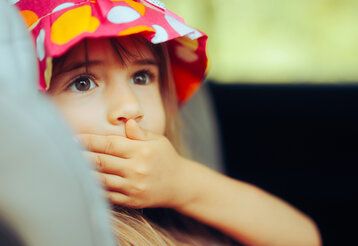 Mädchen mit buntem Hütchen hält sich die Hand vor dem Mund, weil ihm übel ist
