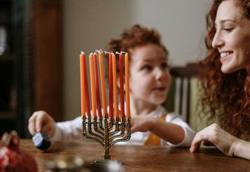 ein achtarmiger Kerzenständer im Vordergrund, dahinter ein Kind mit seiner Mutter an einem Tisch