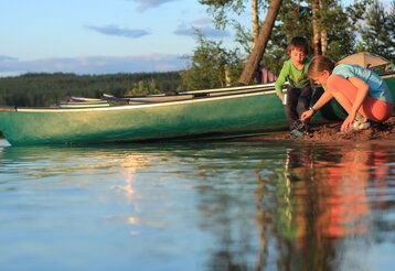 zwei Kinder spielen an einem See im Sand vor einem Boot