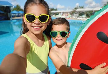 Ein Mädchen und ein Junge sind mit einem großen Schwimmreifen am Hotelpool