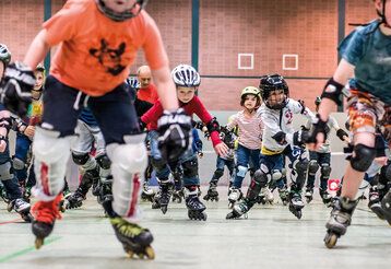 Kinder fahren auf Inlineskates in einer Turnhalle auf den Fotografen zu