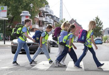 fünf Kinder gehen über einen Zebrastreifen in Düsseldorf, im Hintergrund Häuser und die Fleher Brücke