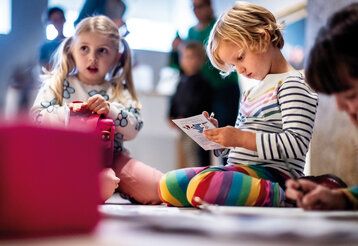 Kinder sitzen im Museum auf dem Boden und beschäftigen sich
