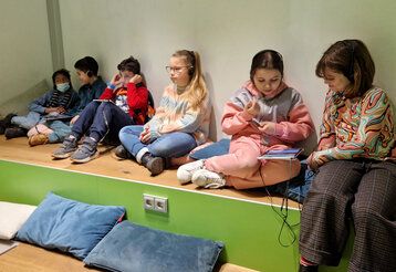 Kinder sitzen auf einem Podest, Düsseldorfer Grundschulkinder bei der Station Kino für die Ohren in der Zentralbibliothek am KAP