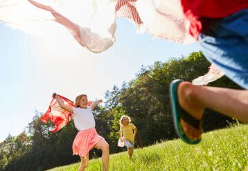 Kinder laufen mit Tüchern über eine Wiese