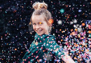 Mädchen im Konfettiregen, lacht, Hintergrund dunkel