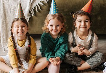 drei Mädchen mit Partyhütchen sitzen lachend vorm Sofa auf dem Boden