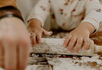 Detailaufnahme von Kinderhänden, die ein bemehltes Nudelholz anfassen