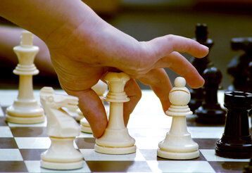 Kinderhand bewegt Dame über ein Schachbrett