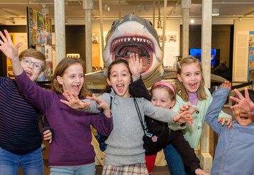 Gruppenbild von Kindern bei der Kindermuseumsnacht im Filmmuseum vor einer Hai-Attrappe