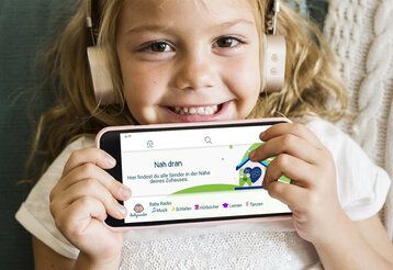 Mädchen mit Kopfhörern hält Smartphone vor sich