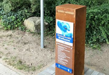 Briefkasten aus rostigem Metall mit Bild von blauem Elefanten am Wegesrand