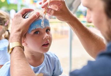 Kinderschminken bei der Einweihung der Kita Flinger Broich, ein Mädchen wird von einem Mann geschminkt