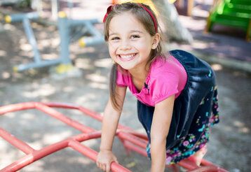 Mädchen klettert auf einem Klettergerüst und lacht in die Kamera