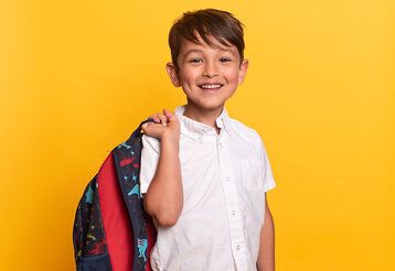 Porträt eines kleinen Jungen mit Schultasche, Hintergrund gelb
