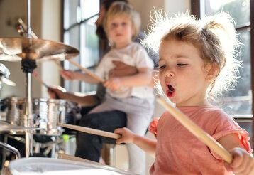 Kleines Mädchen spielt Schlagzeug und singt Vater und Bruder im Hintergrund