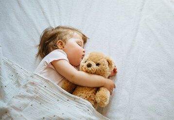 Kleinkind schläft mit Teddy im Arm