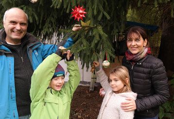 Ein Mann, eine Frau und zwei Kinder stehen bei einer Tanne und schmücken die