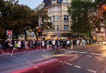 Leute stehen am Büdchentag vor einem Kiosk auf der Volksgartenstraße in Düsseldorf, abendliche Stimmung