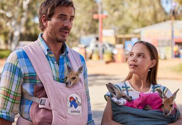Szene aus dem Film Lilly und die Kängurus, ein Mann und ein Mädchen stehen nebeneinander und sprechen, beide tragen Kängurus bei sich