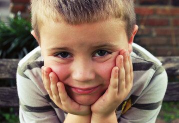 kleiner Junge hat seinen Kopf in die Hände gestützt und schaut in die Kamera