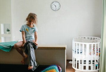 Kleines Mädchen sitzt im Kinderzimmer, zieht sich selbst ihre Hose an.