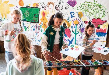 vier Mädchen malen zusammen an einem großen Bild