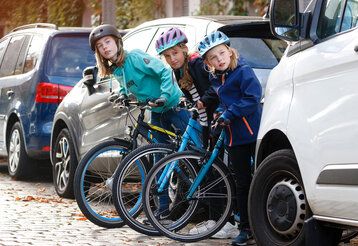 Mädchen auf Rädern schauen zwischen geparkten Autos hervor