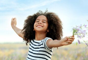 Porträt eines Mädchens, das in einem Feld steht, die Arme ausbreitet und sich freut