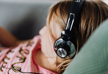 Mädchen liegt mit Kopfhörern auf einem Kissen, das Mädchen ist unscharf, der Kopfhörer scharf