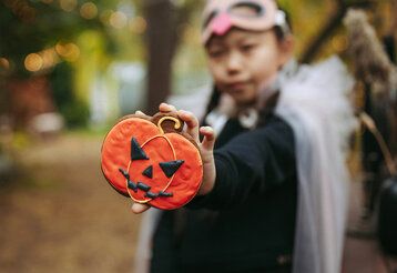 ein verkleidetes Mädchen hält einen Kürbis-Keks in die Kamera