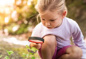 Mädchen guckt sich mit einer Lupe eine Pflanze an